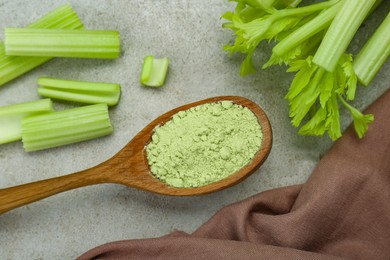 Photo of Natural celery powder in wooden spoon and fresh stalks on grey table, flat lay