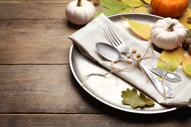 Autumn table setting with pumpkins and fallen leaves on wooden background, closeup. Space for text