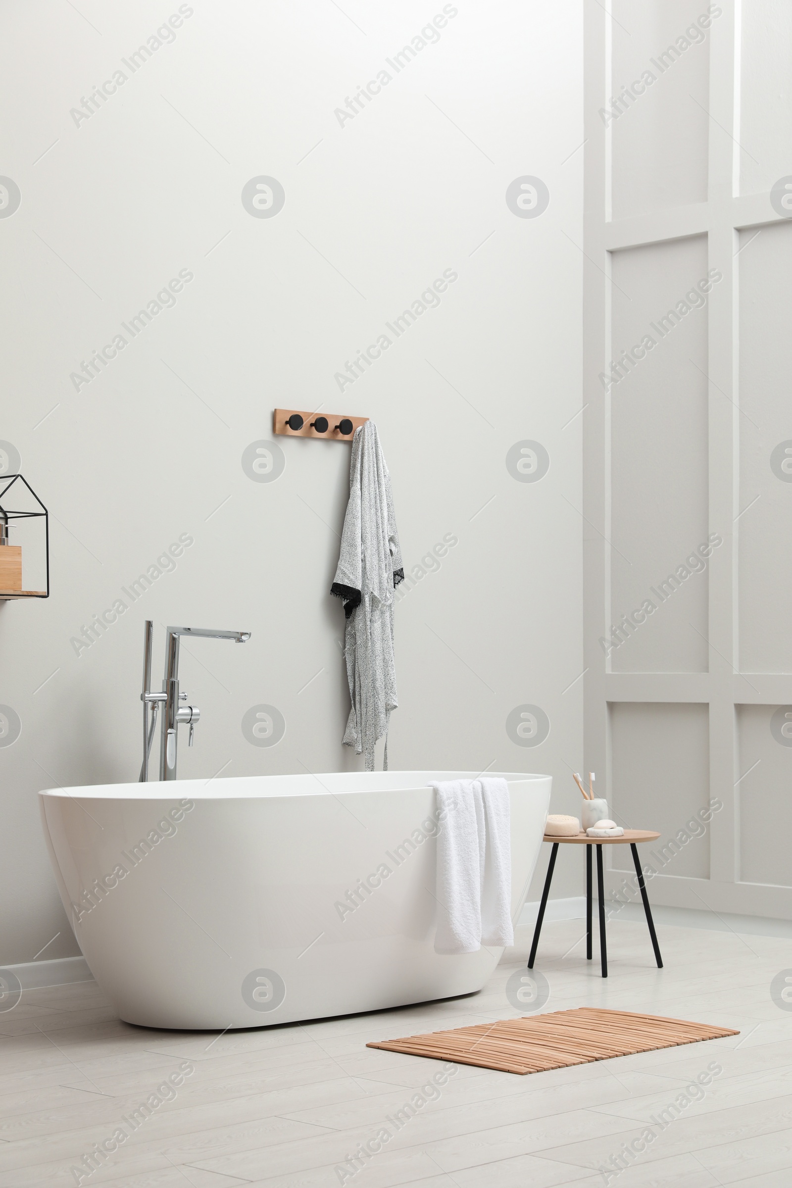 Photo of Modern ceramic bathtub with towel near white wall in room