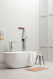 Modern ceramic bathtub with towel near white wall in room