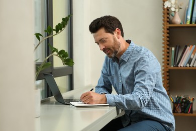 Photo of Man writing something and laptop at table in cafe