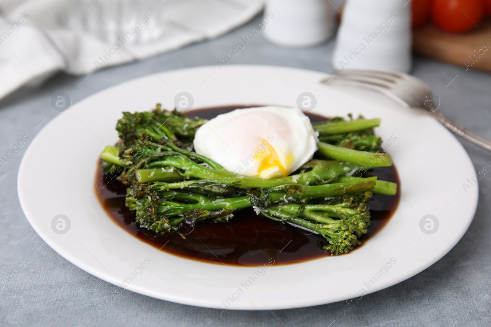 Photo of Tasty cooked broccolini with poached egg and sauce on grey table, closeup