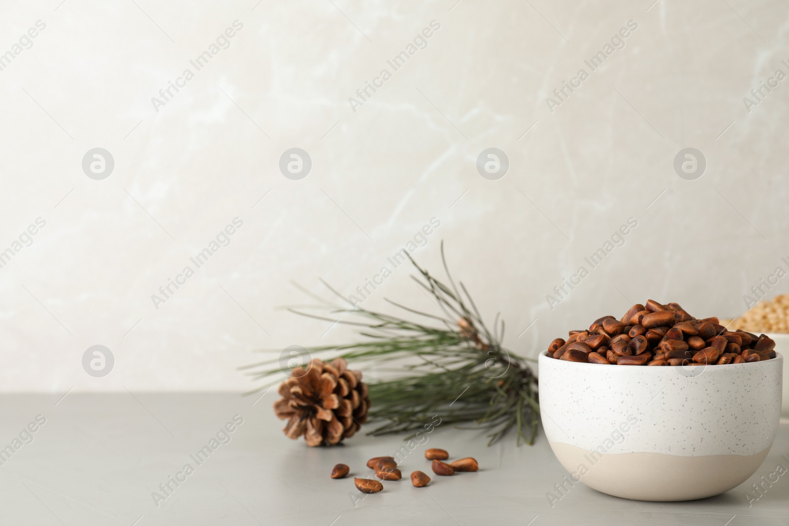 Photo of Bowl with pine nuts on table against light background. Space for text