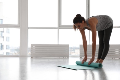 Photo of Young woman unrolling mat in yoga studio