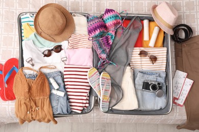 Photo of Open suitcase with summer clothes, accessories and shoes on bed, flat lay