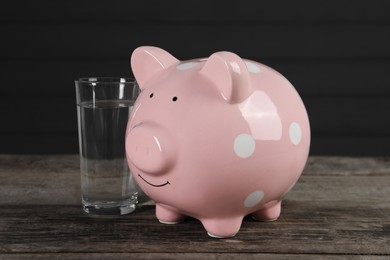 Photo of Water scarcity concept. Piggy bank and glass of drink on wooden table