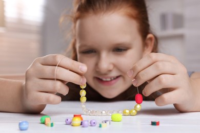 Cute girl making beaded jewelry at table in room, focus on hands