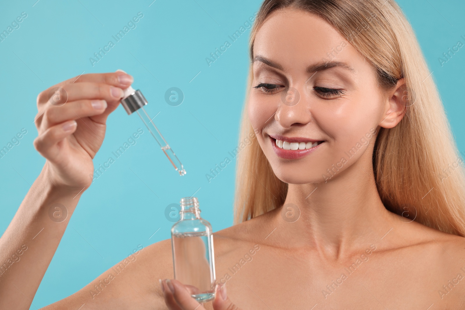 Photo of Beautiful woman with cosmetic serum in her hands on light blue background