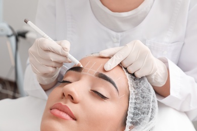 Photo of Young woman getting prepared for procedure of permanent eyebrow makeup in tattoo salon, closeup