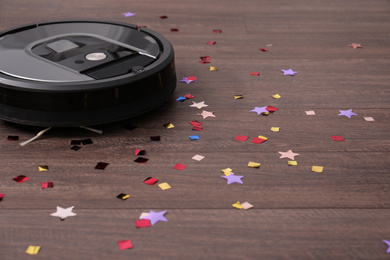 Modern robotic vacuum cleaner removing confetti from wooden floor. Space for text