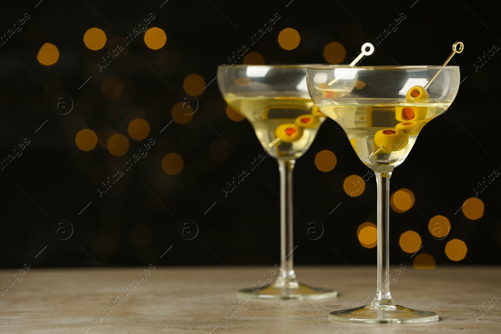 Photo of Glasses of Classic Dry Martini with olives on grey table against blurred background. Space for text