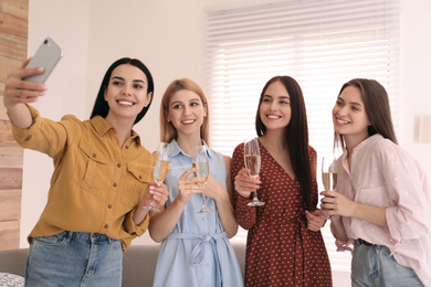 Photo of Beautiful young ladies with champagne taking selfie at home. Women's Day