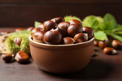 Photo of Fresh sweet edible chestnuts on brown wooden table, closeup