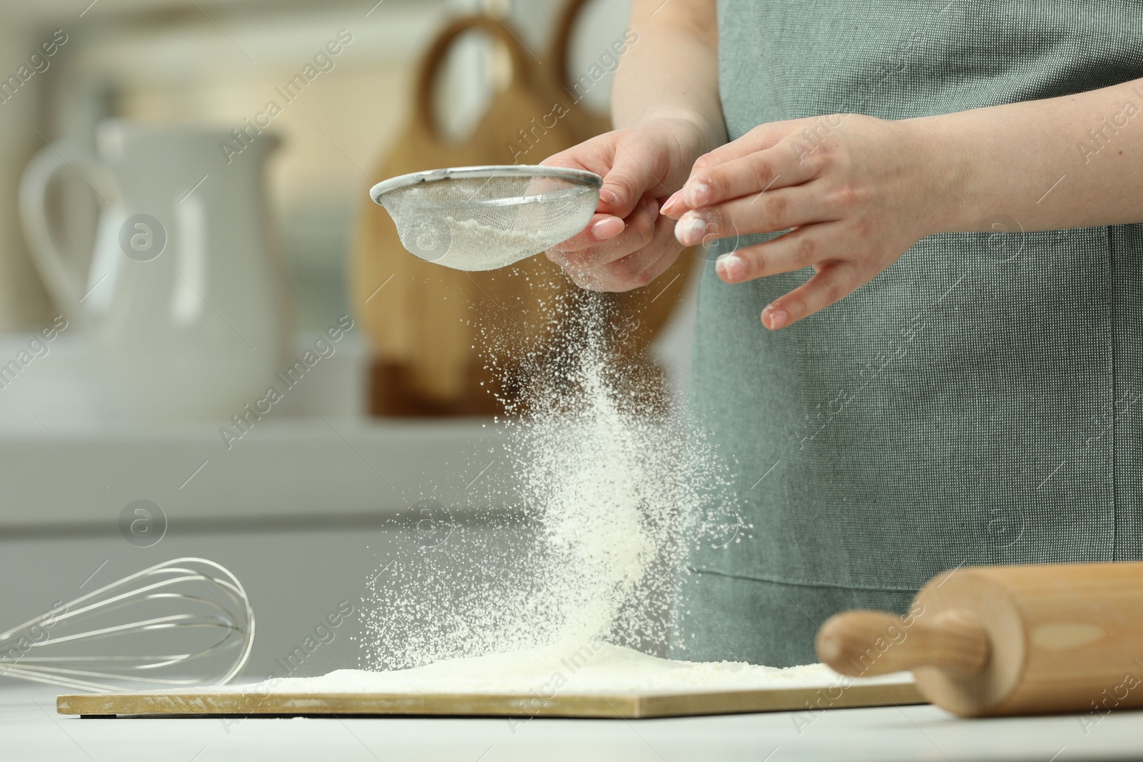 Photo of Woman sieving flour at table in kitchen, closeup. Space for text