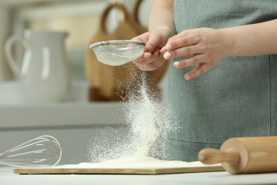 Woman sieving flour at table in kitchen, closeup. Space for text