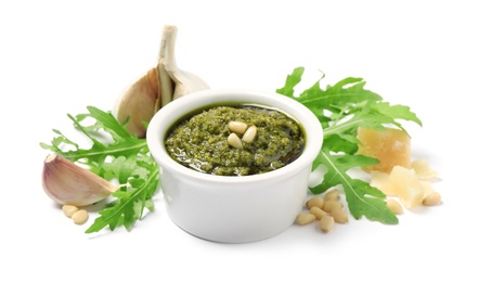 Bowl of tasty arugula pesto and ingredients on white background