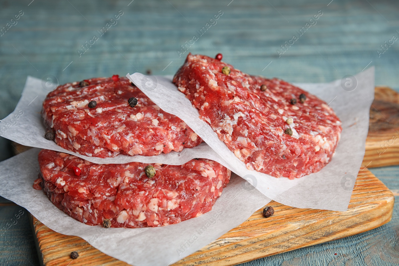 Photo of Raw meat cutlets for burger on blue wooden table, closeup