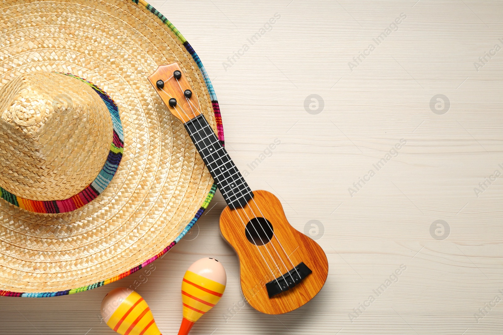 Photo of Mexican sombrero hat, maracas and guitar on white wooden background, flat lay. Space for text