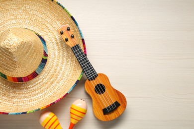 Mexican sombrero hat, maracas and guitar on white wooden background, flat lay. Space for text