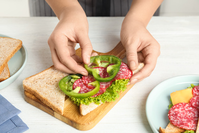 Photo of Woman making sandwich with green bell pepper and sausage at white table, closeup