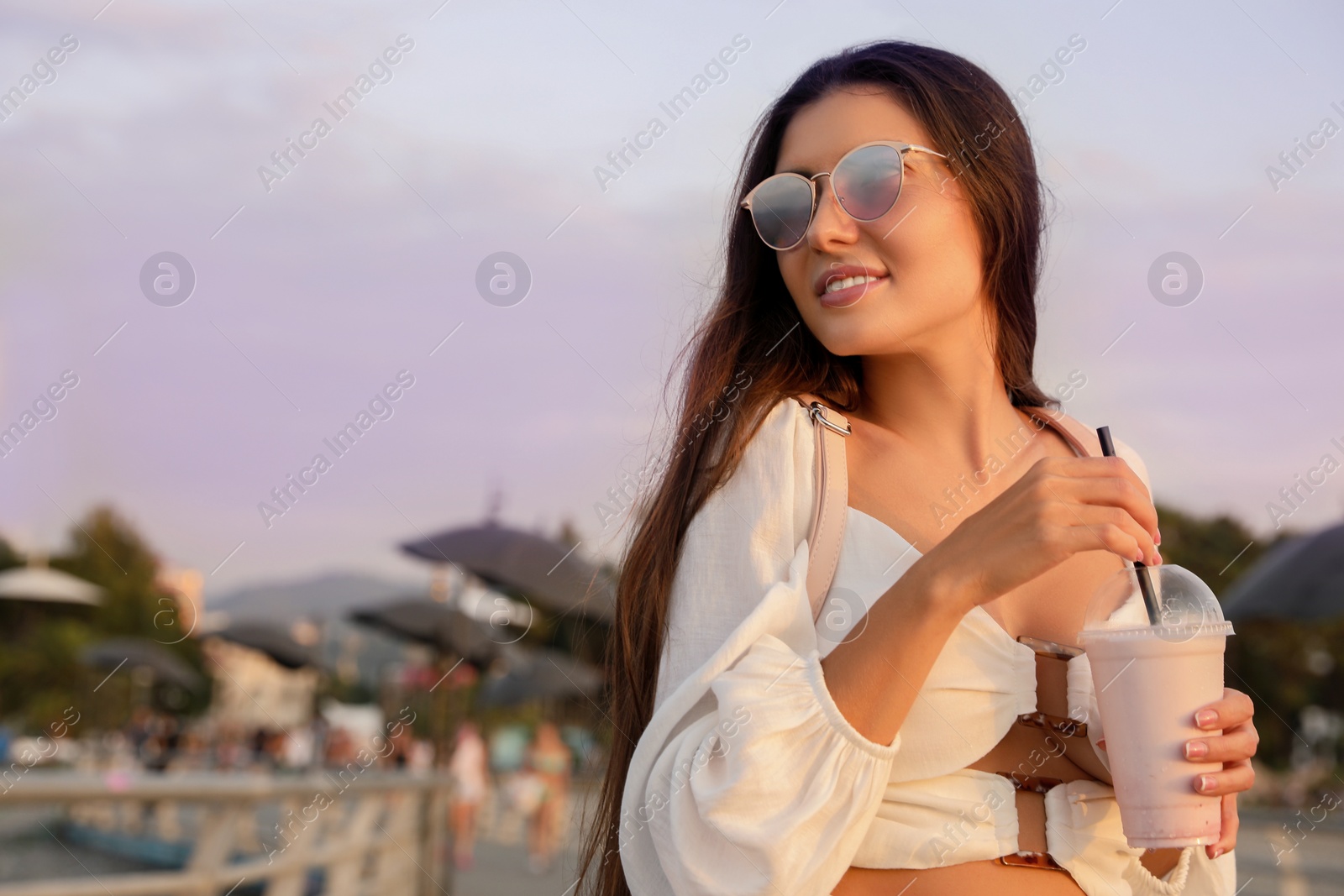 Photo of Beautiful young woman with tasty milk shake outdoors, space for text