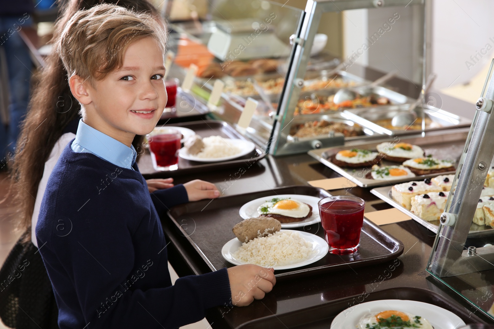 Photo of Cute boy near serving line with healthy food in school canteen