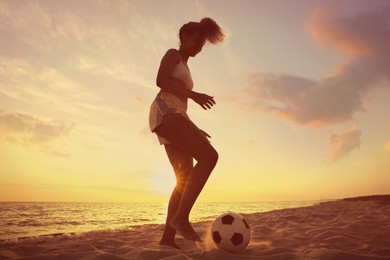 Photo of African American woman playing football on beach at sunset