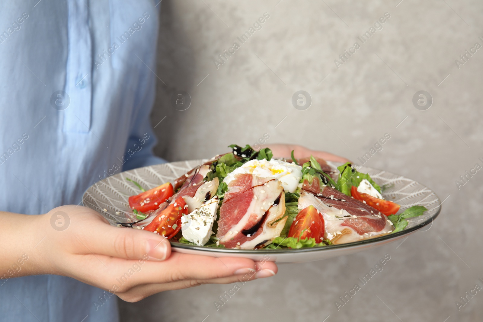 Photo of Woman holding plate with delicious prosciutto salad on grey background, closeup