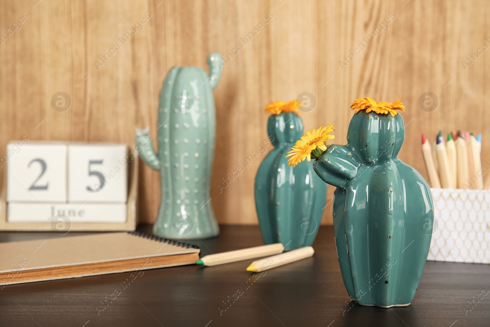 Photo of Trendy cactus shaped vases and stationery on table against wooden background. Creative decor