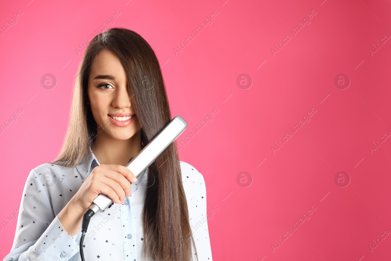 Photo of Happy woman using hair iron on color background. Space for text