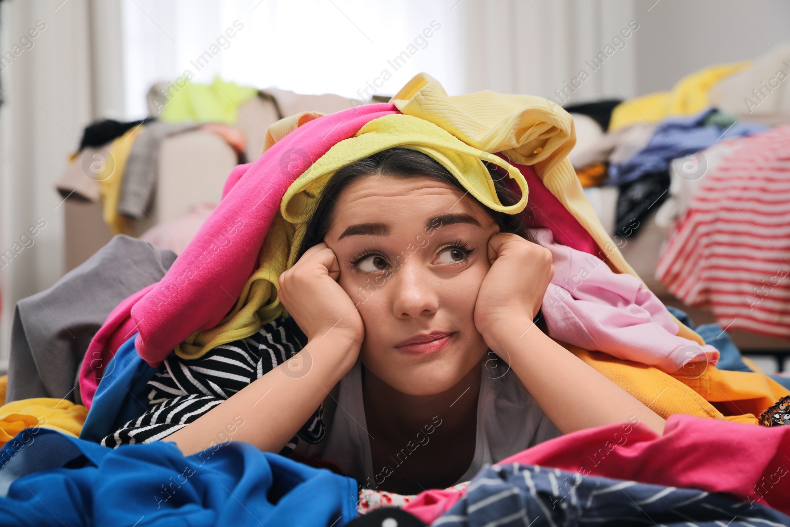 Photo of Pensive young woman with lots of clothes on floor in room. Fast fashion