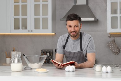 Photo of Happy man cooking by recipe book in kitchen