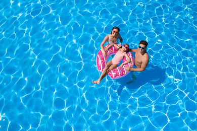 Image of Happy family with inflatable ring in swimming pool, space for text. Summer vacation
