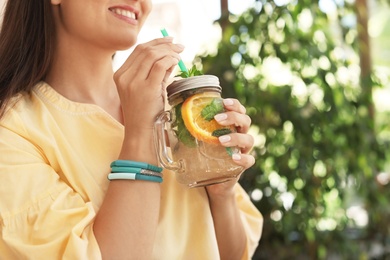 Photo of Young woman with mason jar of tasty natural lemonade in cafe, closeup. Detox drink