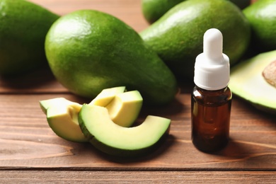 Bottle with oil and fresh avocados on wooden table