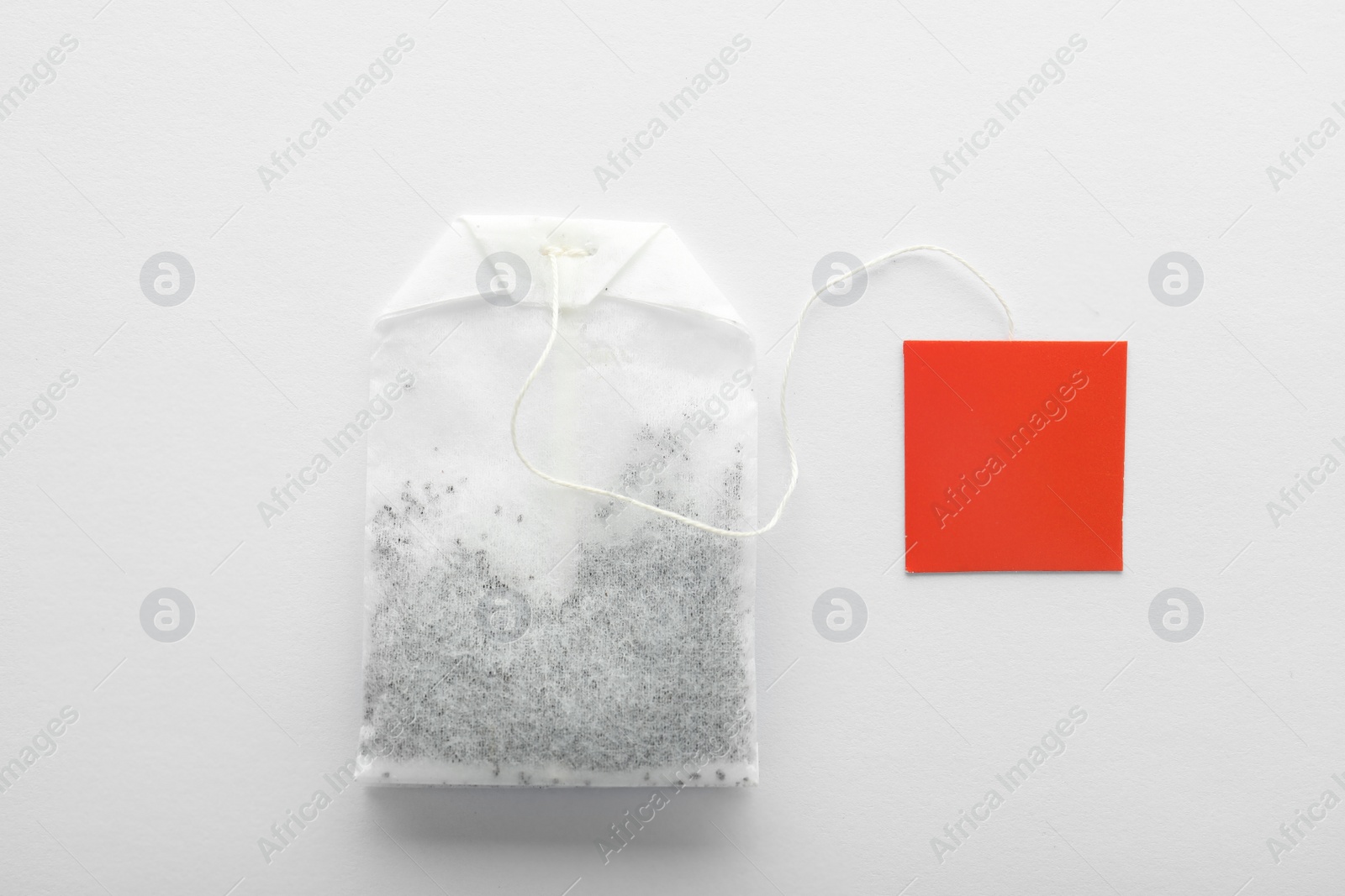 Photo of Unused tea bag with tag on white background, top view. Space for text