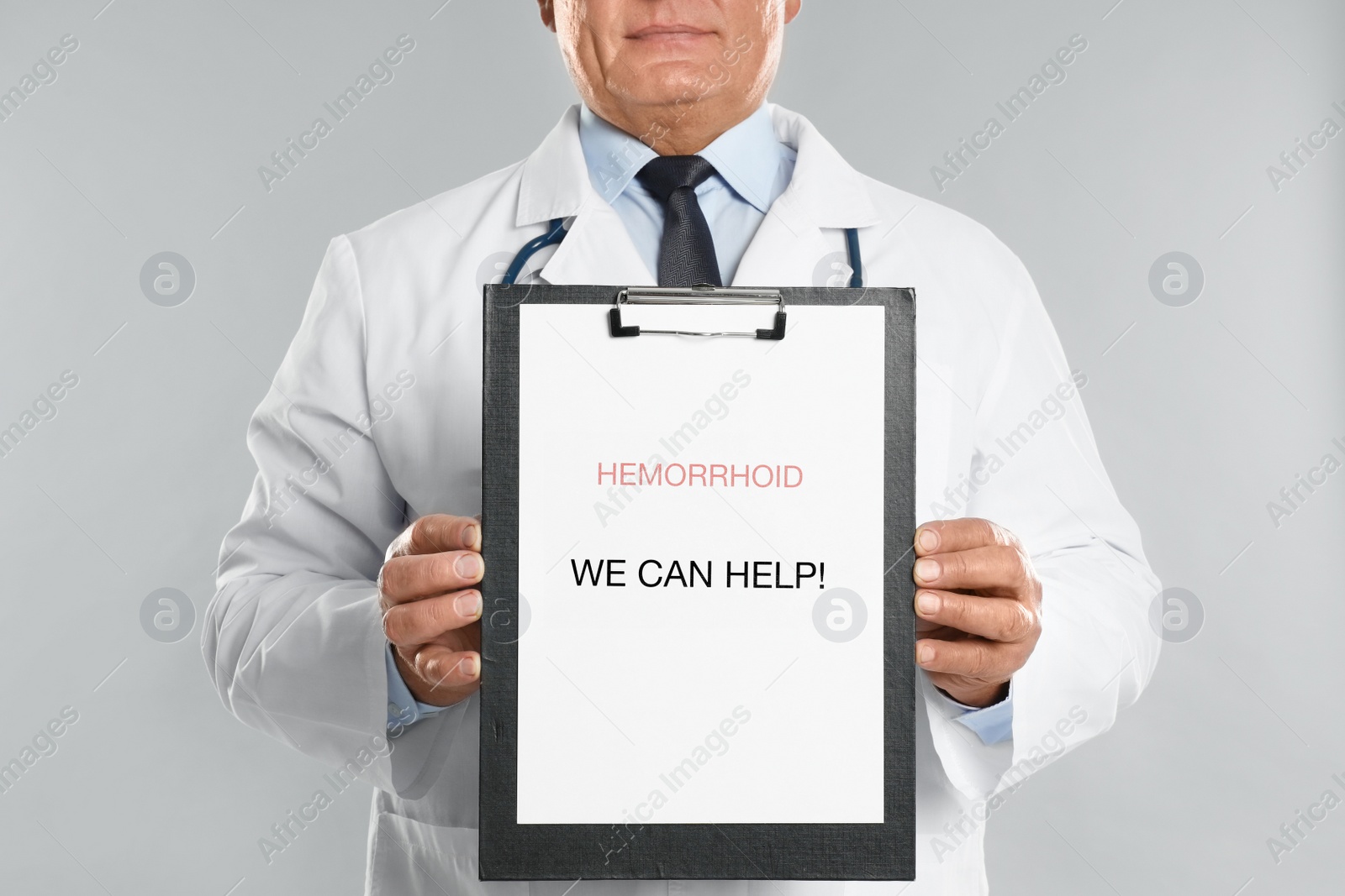 Photo of Doctor holding clipboard with words HEMORRHOID WE CAN HELP on light grey background, closeup