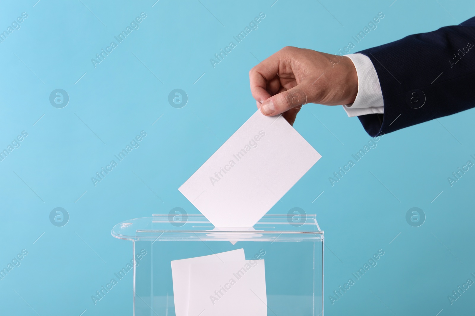 Photo of Man putting his vote into ballot box on light blue background, closeup