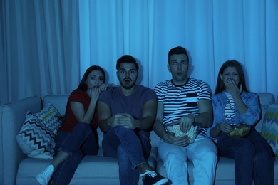 Photo of Group of people with snacks watching TV together on couch in dark room