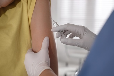 Doctor vaccinating young woman against Covid-19 in clinic, closeup