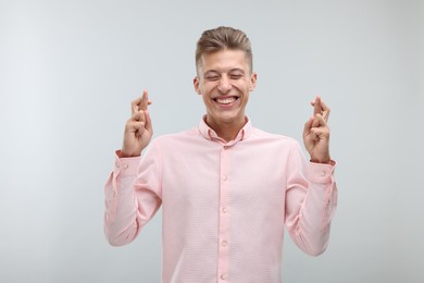 Photo of Happy young man crossing his fingers on light grey background