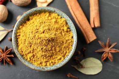 Dry curry powder in bowl and other spices on dark table, flat lay