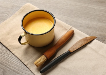 Photo of Mug of melting butter, brush and knife on table. Space for text