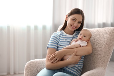 Mother with her cute baby in armchair at home, space for text