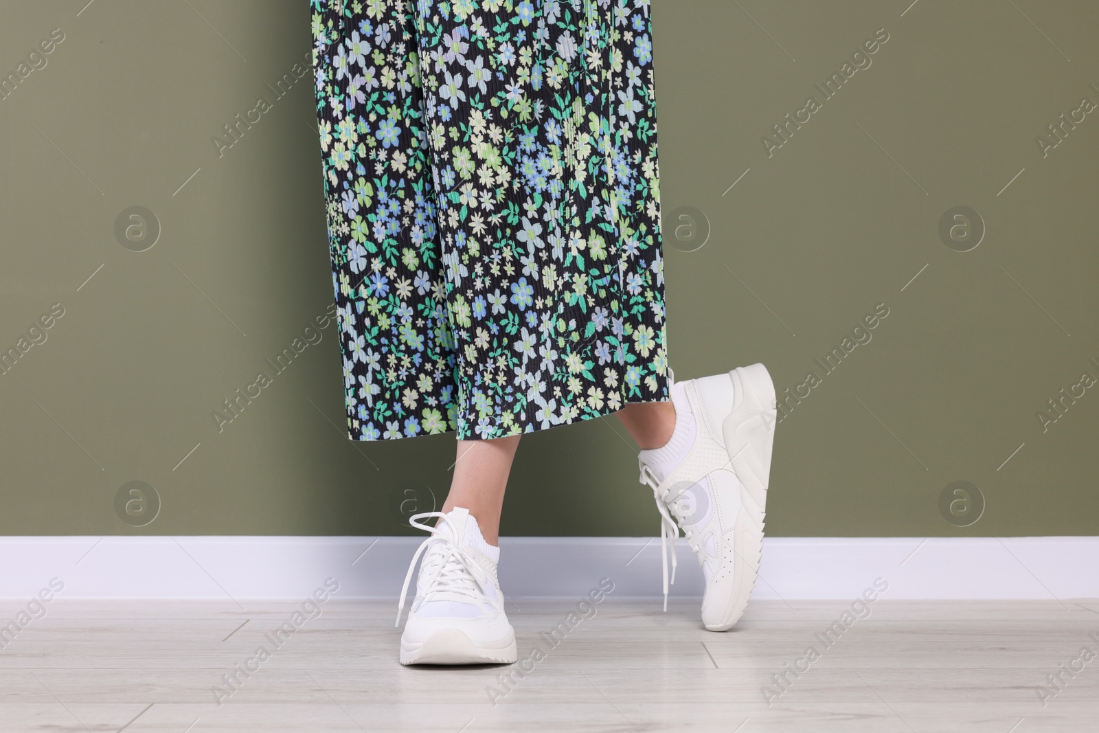 Photo of Woman wearing pair of new stylish sneakers near dark olive wall, closeup