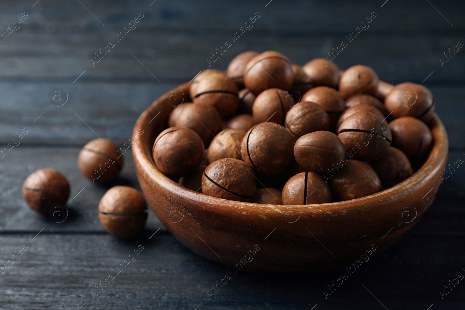 Photo of Bowl with organic Macadamia nuts on blue wooden background