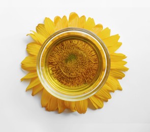 Bowl of sunflower oil and flower on white background, top view