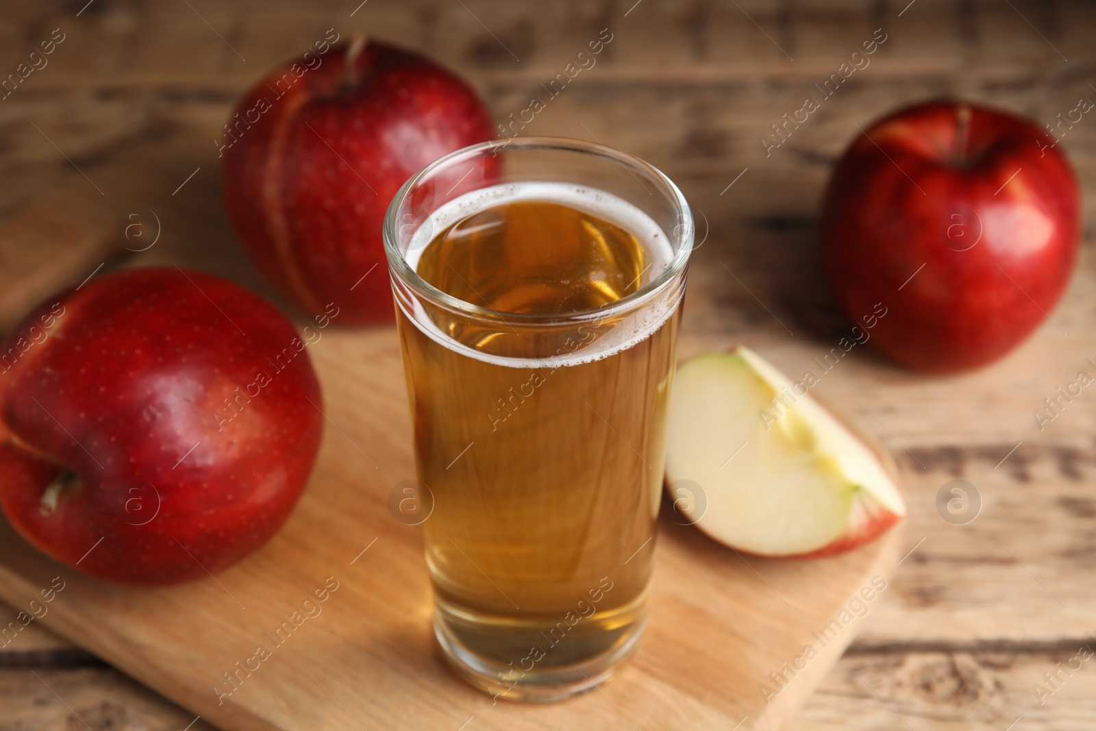 Photo of Glass of delicious cider and ripe red apples on wooden table