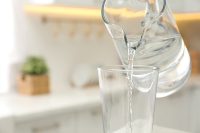 Photo of Pouring water from jug into glass in kitchen, closeup. Space for text
