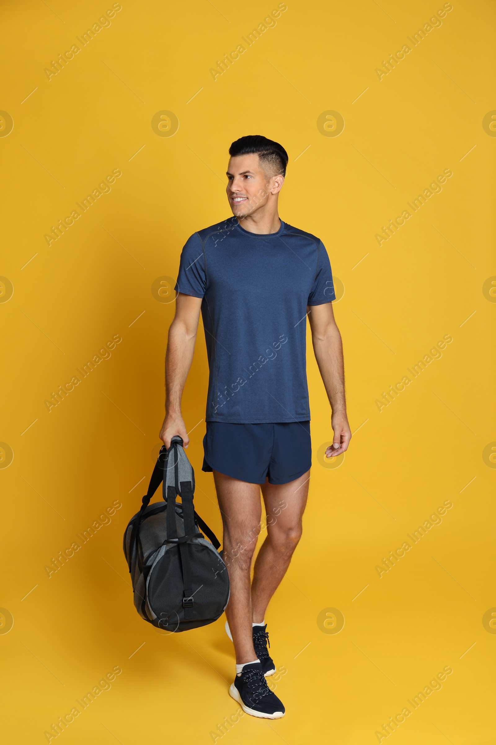 Photo of Handsome man with sports bag on yellow background